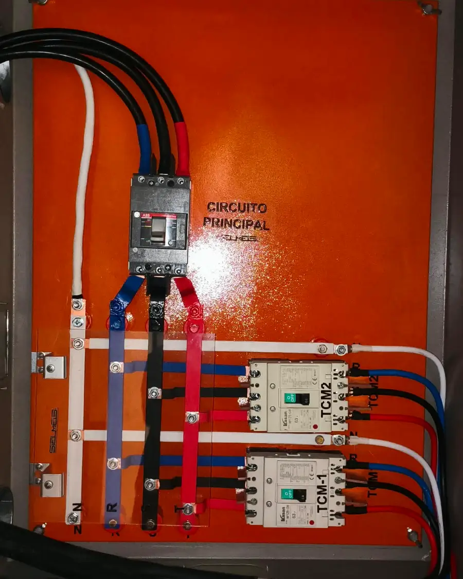 Tablero de centralización de medidores TCMS ejecutado por SIELMEIS en Cochabamba: interruptor principal ABB de caja moldeada, barras de cobre N, R, S y T, y dos disyuntores de 63 A rotulados TCM-1 y TCM-2